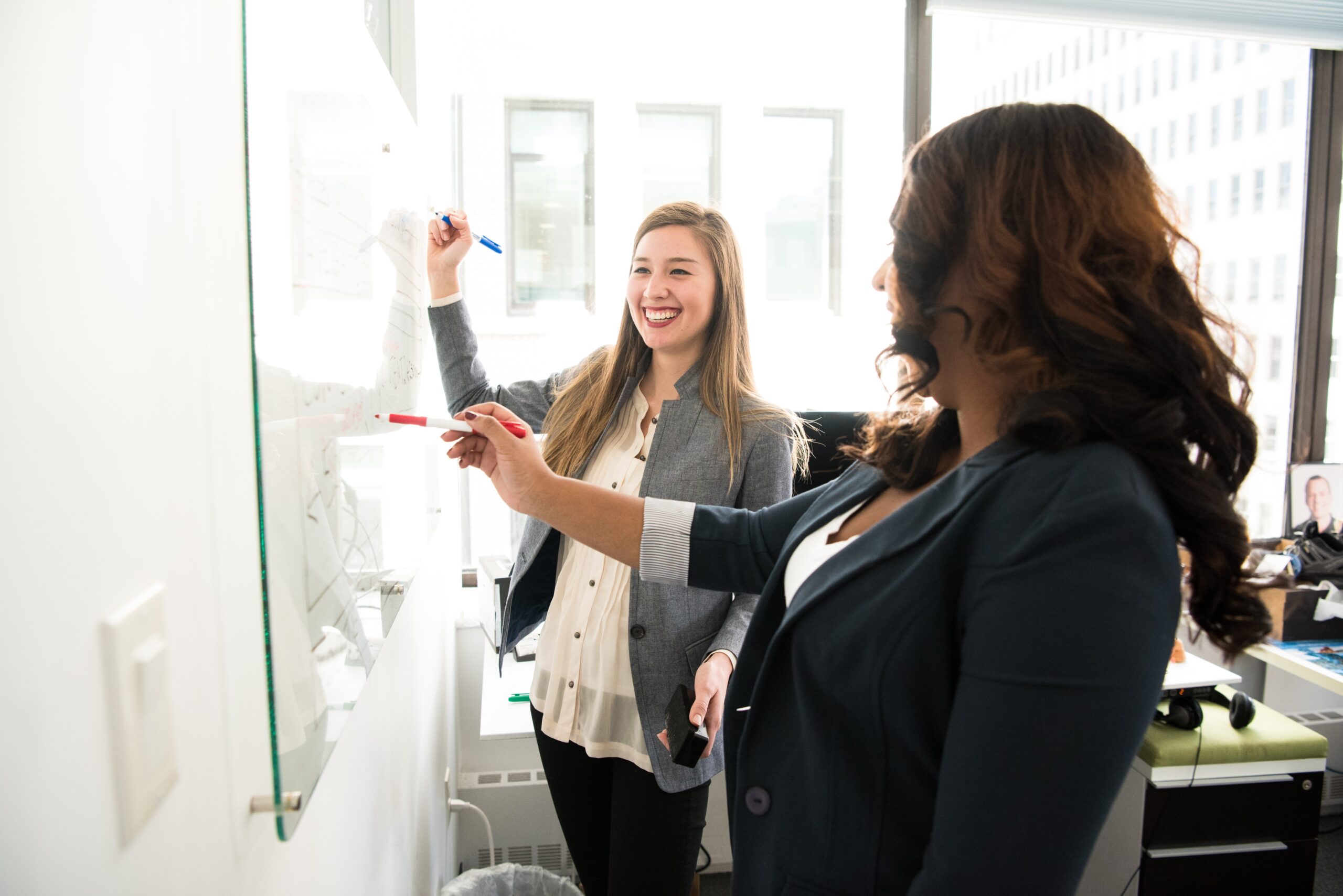 Two women smiling writing on a white board