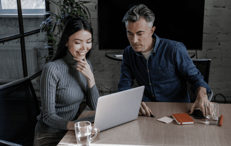 A woman and a man sat as a desk looking at a laptop.